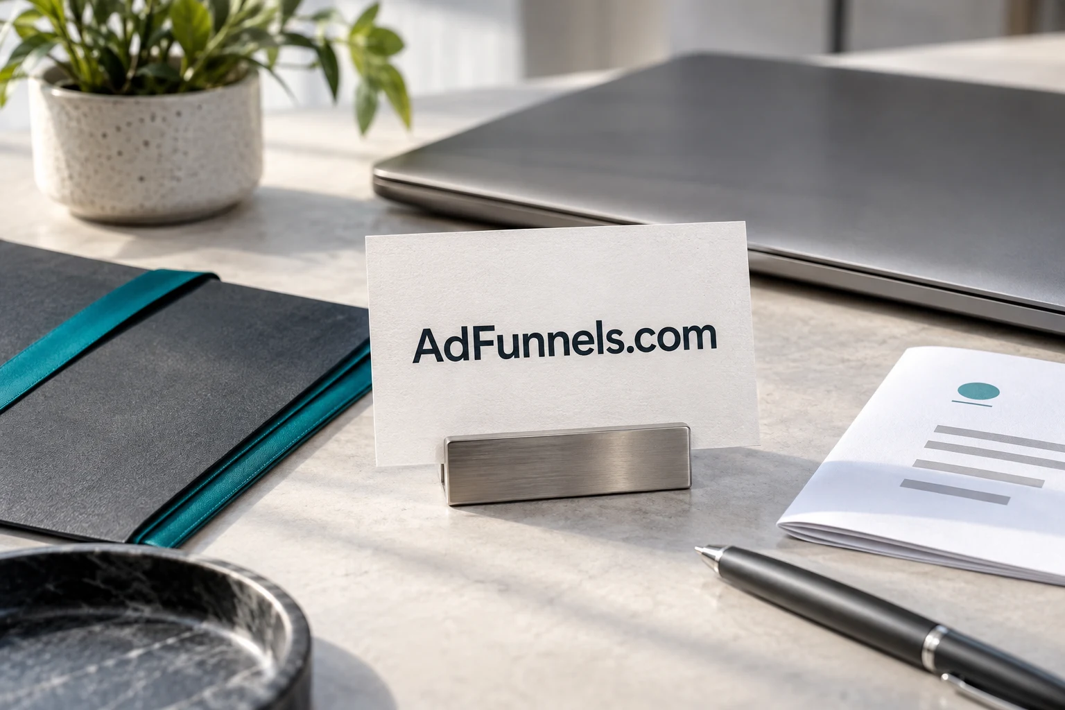 AdFunnels.com card beside graphite stationery and a brushed-metal laptop
